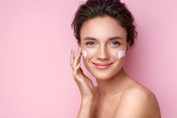 Woman with face cream glowing in pink background